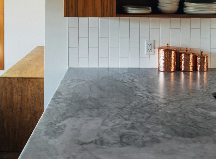 A polished Tundra Grey marble countertop in a modern kitchen with white tiled backsplash and wooden cabinets.