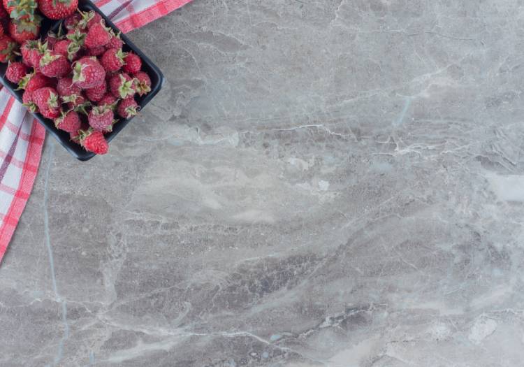 An image showcasing the intricate patterns of Tundra Grey Marble, adorned with a container of fresh strawberries on a checkered cloth.