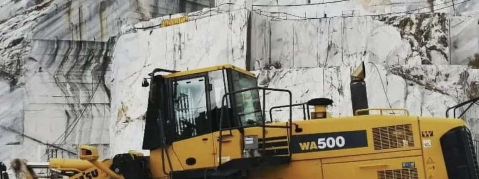 Komatsu excavator at a granite quarry with large white granite blocks in the background
