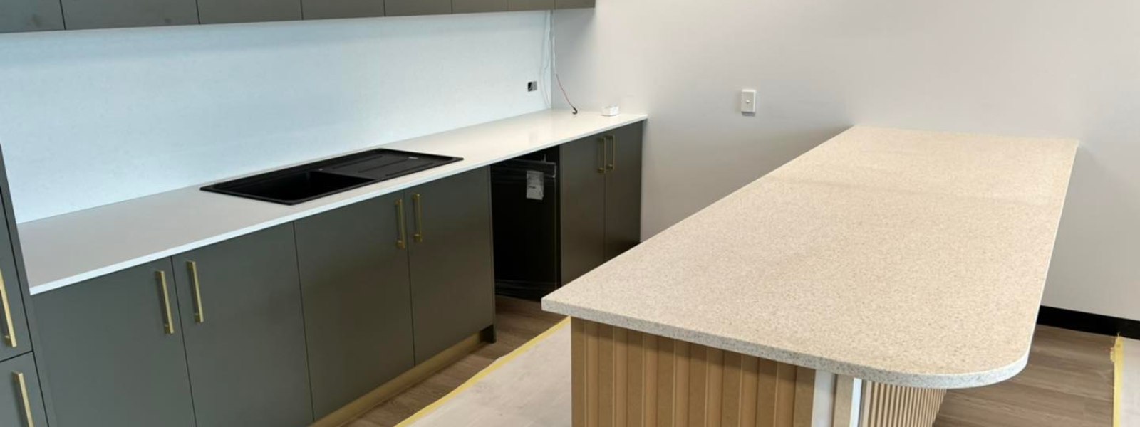 Kitchen with Terrazzo countertop, featuring dark cabinets with gold handles and a large island.