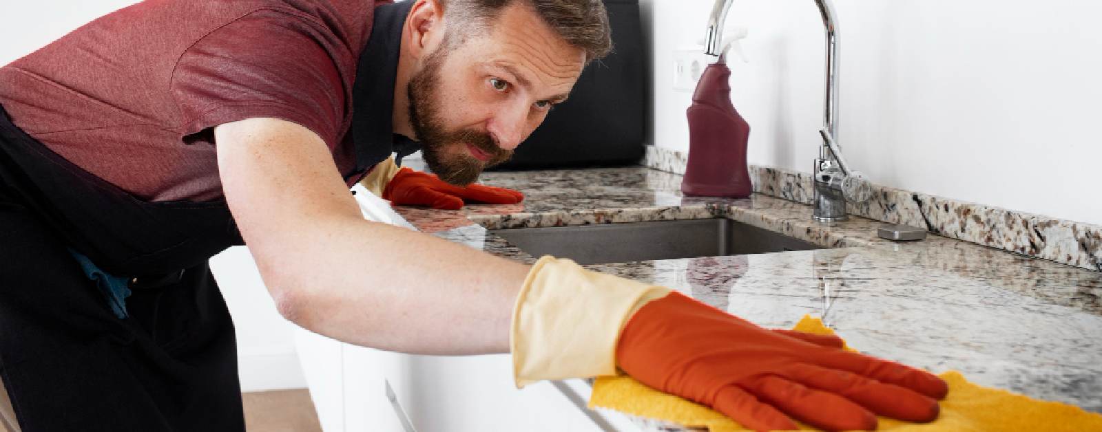 Man in gloves meticulously cleaning a porcelain kitchen countertop with a yellow cloth.