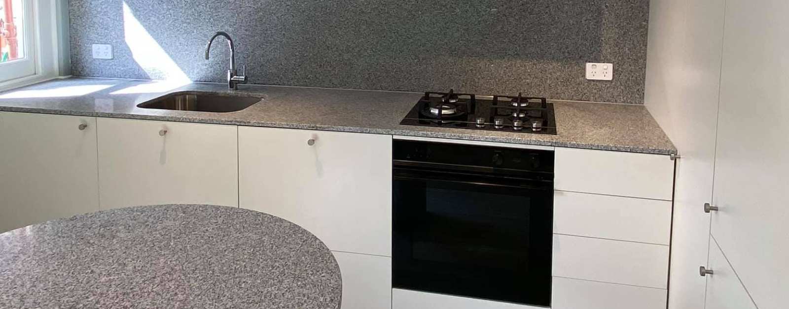 Modern kitchen design featuring grey granite countertops, backsplash, and a round kitchen island.