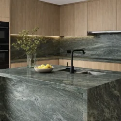 Kitchen featuring a Verde Fusion granite waterfall island and matching slab backsplash with light wood cabinetry.